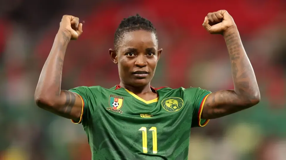 Marie Ngah Manga, wearing a green Cameroon shirt with a yellow number 11 on the chest, holds up both arms with fists clenched in celebration